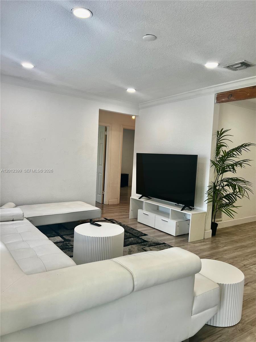 A living room features a white sectional sofa, a television on a stand, and wood-look flooring — 12040 N Miami Ave, North Miami FL 33168, NORTH MIAMI, FL