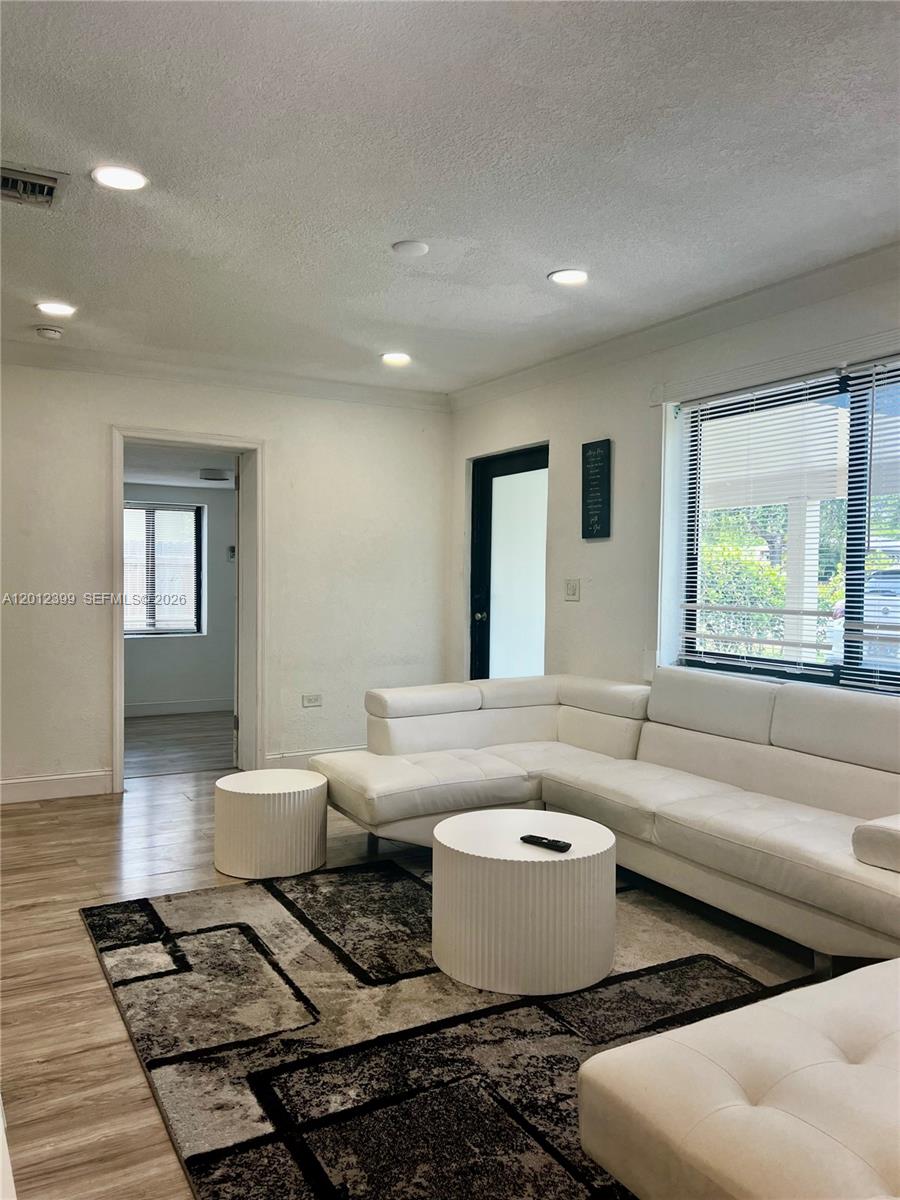 A living room features a white sectional sofa, two cylindrical tables, and a patterned rug — 12040 N Miami Ave, North Miami FL 33168, NORTH MIAMI, FL