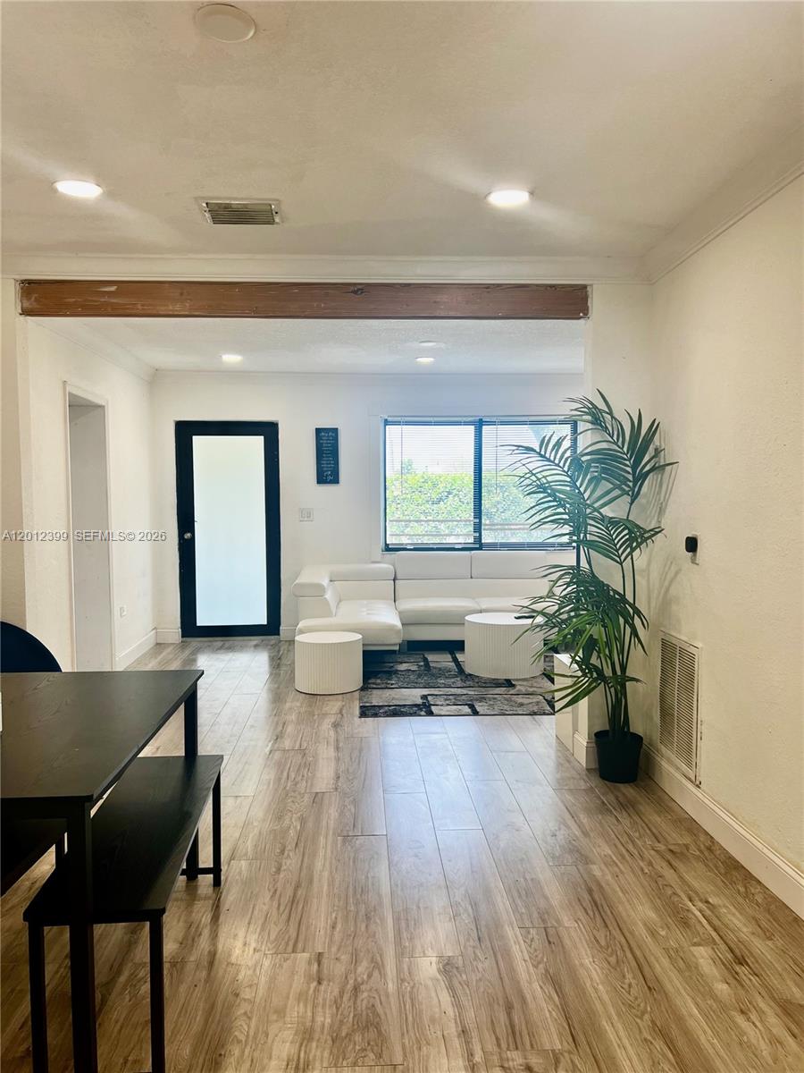 A living room with wood-look flooring features a white sectional sofa and a dining area — 12040 N Miami Ave, North Miami FL 33168, NORTH MIAMI, FL