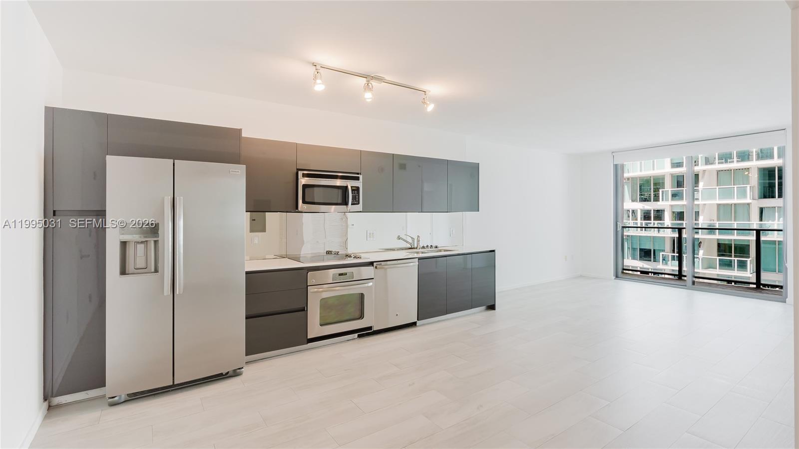 A modern kitchen with gray cabinetry and stainless steel appliances opens into a living area — 31 SE 6th St # 1906, Miami FL 33131, MIAMI, FL