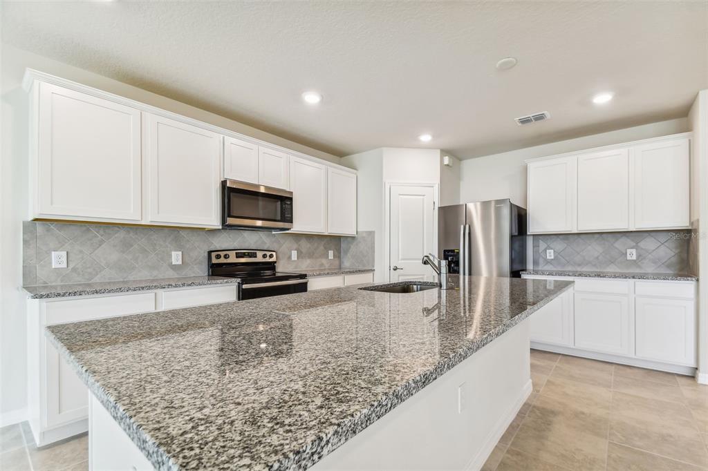 A modern kitchen features white cabinets, stainless steel appliances, and a large central island — 11250 SYCAMORE GLEN LOOP, THONOTOSASSA, FL