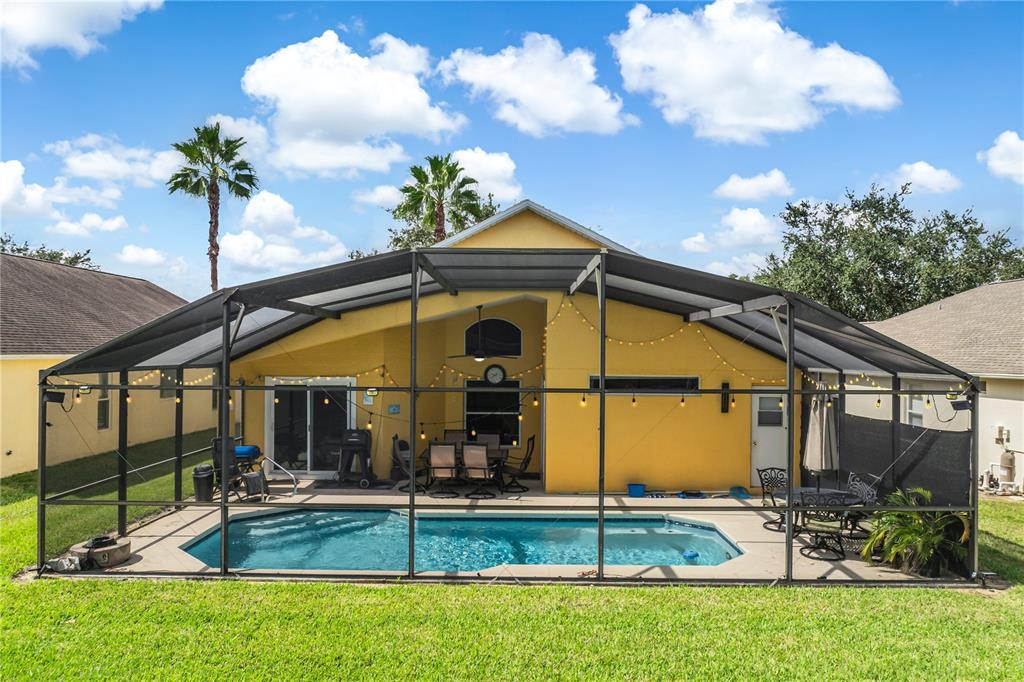 A yellow house features a screened-in pool enclosure with a patio and string lights — 134 LANGHAM DRIVE, DAVENPORT, FL