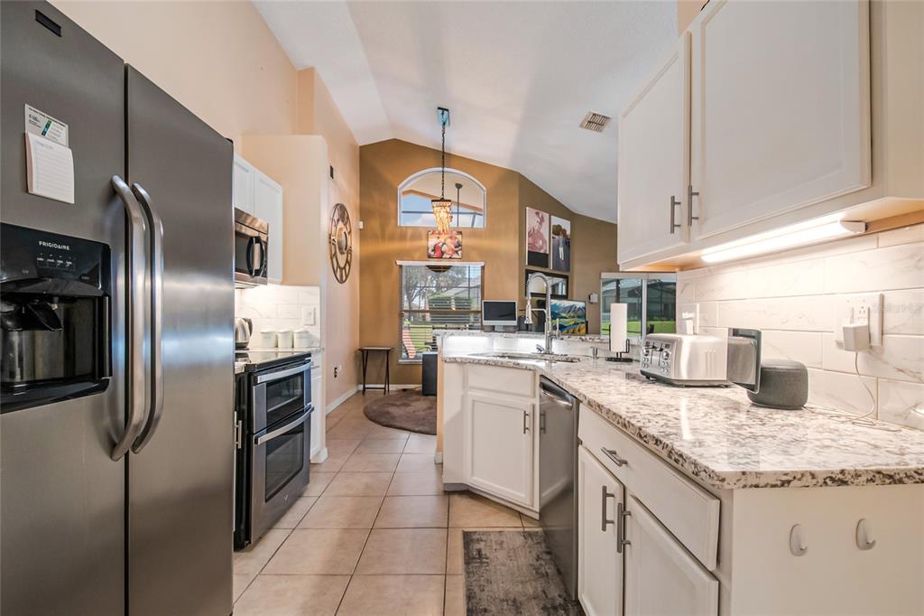 A kitchen with white cabinets, granite countertops, stainless steel appliances, and a vaulted ceiling — 134 LANGHAM DRIVE, DAVENPORT, FL
