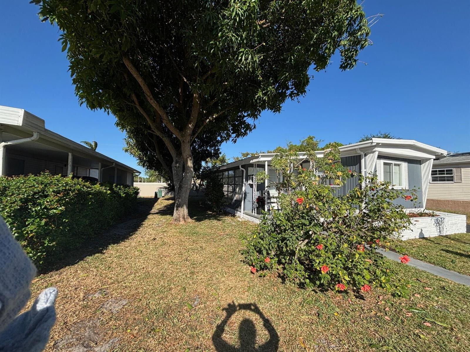 A grassy yard sits between two mobile homes under a large, leafy tree — 6931 NW 45th Terrace, Coconut Creek FL 33073, COCONUT CREEK, FL