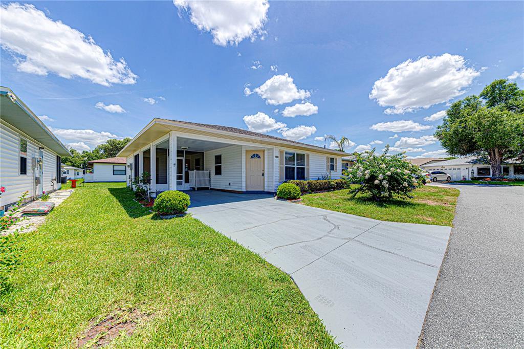 A single-story house with a carport, light siding, and a concrete driveway under a blue sky — 1618 COLONNADES CIRCLE N, LAKELAND, FL