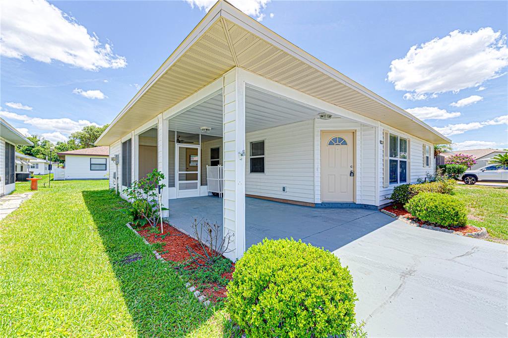 A covered patio with a concrete floor, white siding, and a tan entry door — 1618 COLONNADES CIRCLE N, LAKELAND, FL