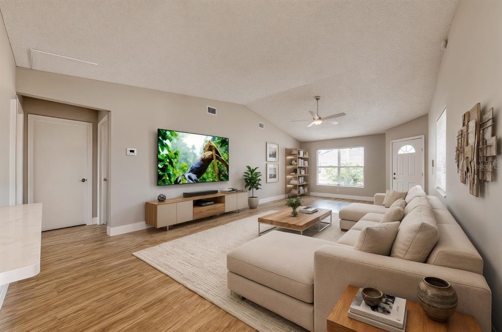 A living room features a sectional sofa, a wall-mounted television, and wood-look flooring — 1618 COLONNADES CIRCLE N, LAKELAND, FL