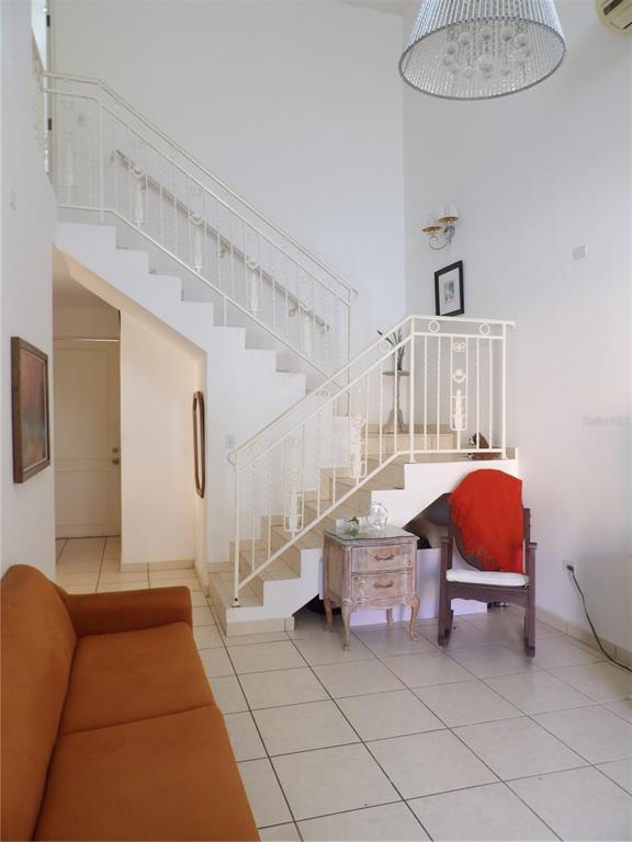 A living room features a white staircase with decorative railings, tile flooring, and a chandelier — Brighton Boulevard A11, DORADO, PR