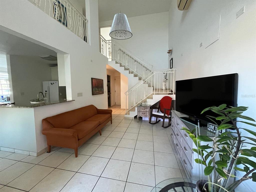 A living room features a tan sofa, a staircase, and a large television on a dresser — Brighton Boulevard A11, DORADO, PR