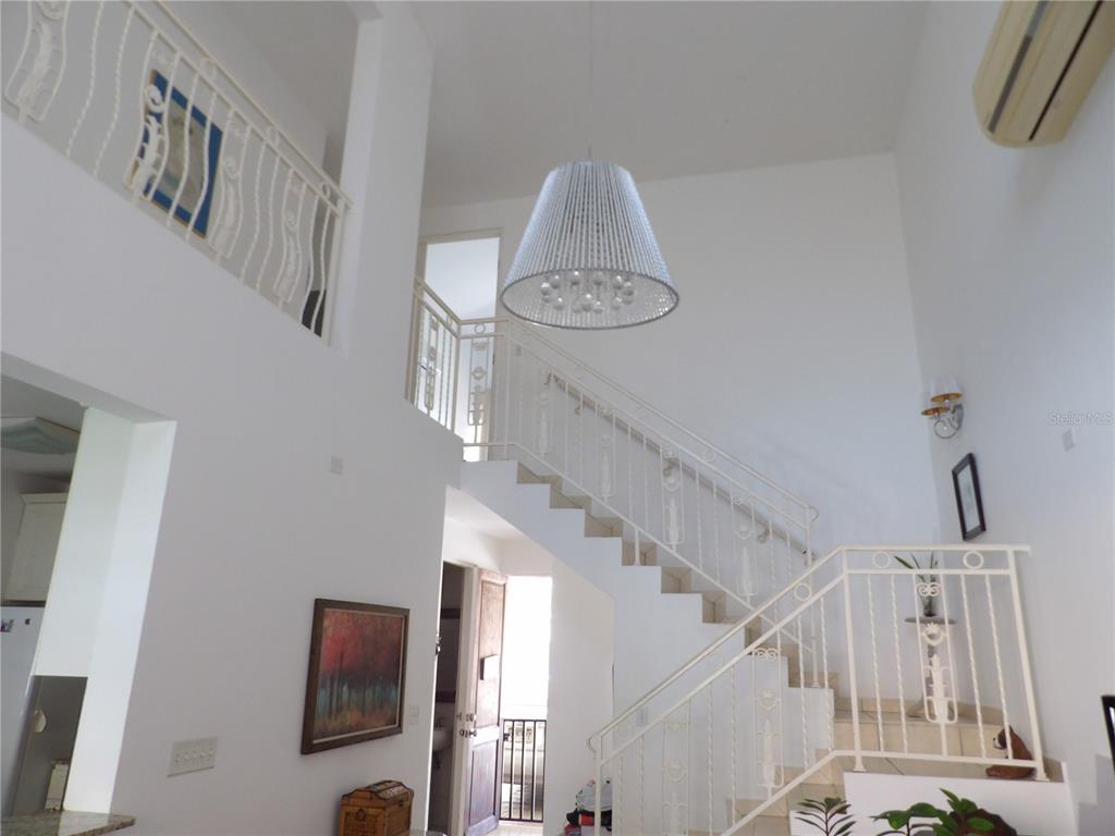 A high-ceilinged foyer features a white staircase with decorative metal railings and a pendant light — Brighton Boulevard A11, DORADO, PR
