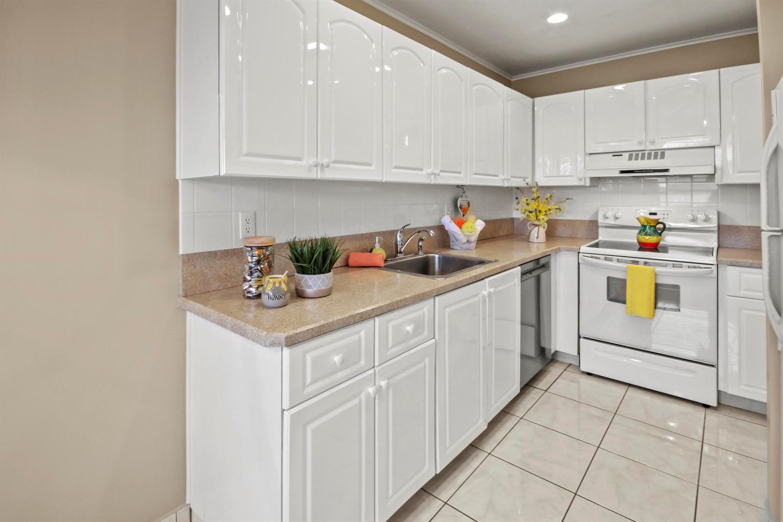A kitchen features white cabinets, tan countertops, a stainless steel sink, and white appliances — 1421 NW 20th Avenue # 204, Delray Beach FL 33445, DELRAY BEACH, FL