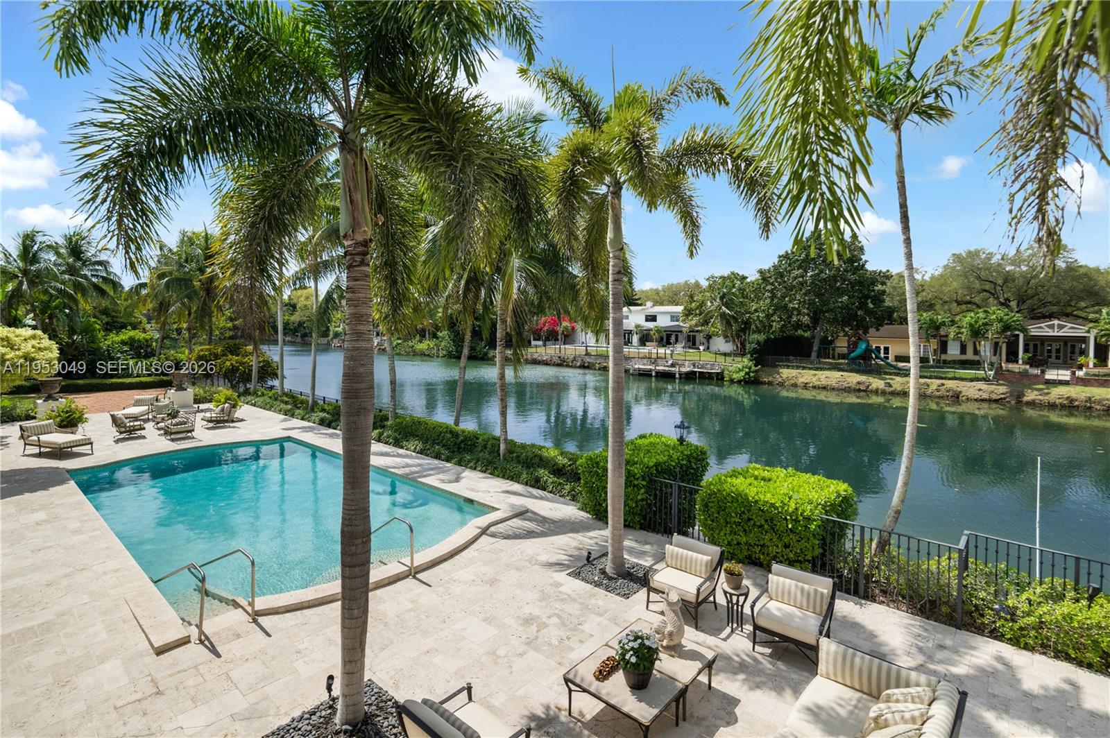 A swimming pool and patio area overlook a canal lined with palm trees and houses — 4620 Granada Blvd, Coral Gables FL 33146, CORAL GABLES, FL
