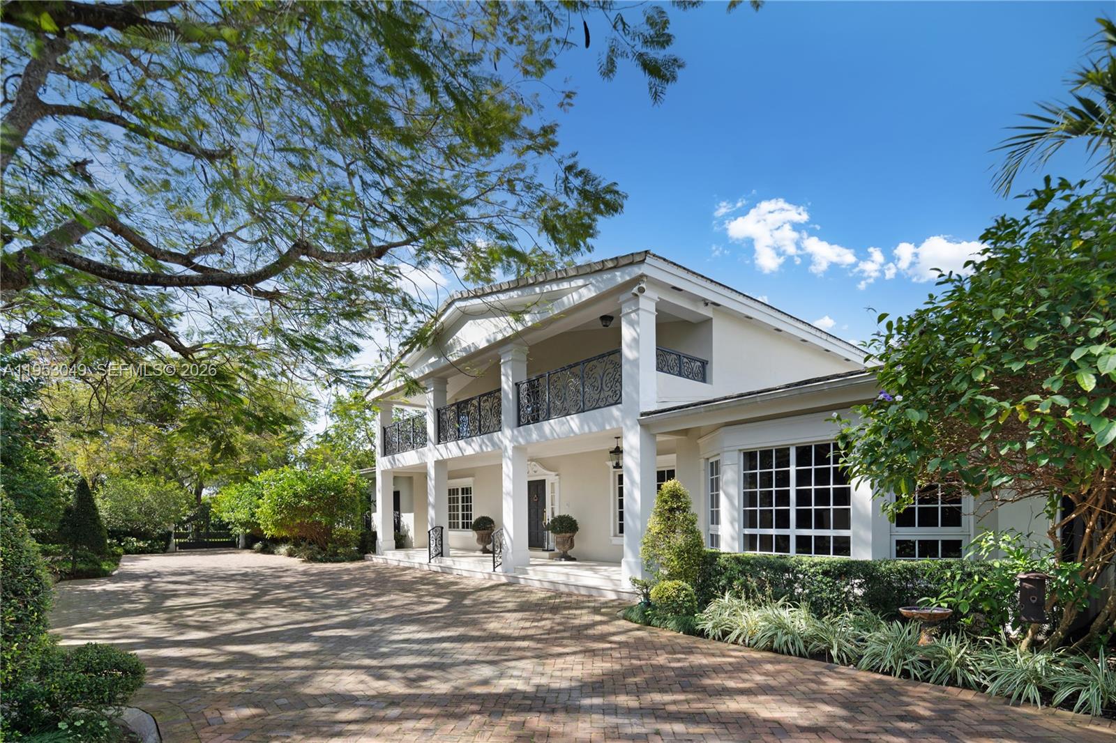 A two-story white house features a brick driveway, a covered porch, and wrought-iron balcony railings — 4620 Granada Blvd, Coral Gables FL 33146, CORAL GABLES, FL