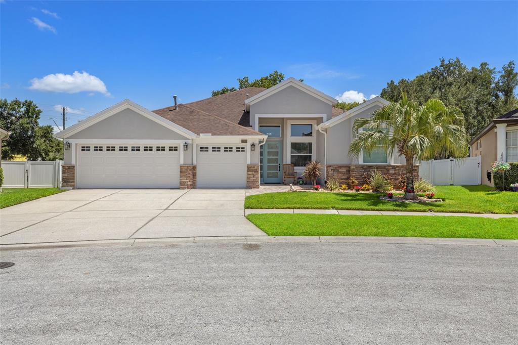 A single-story house with a three-car garage, stone accents, and a light blue front door — 27901 SUMMER PLACE DRIVE, WESLEY CHAPEL, FL