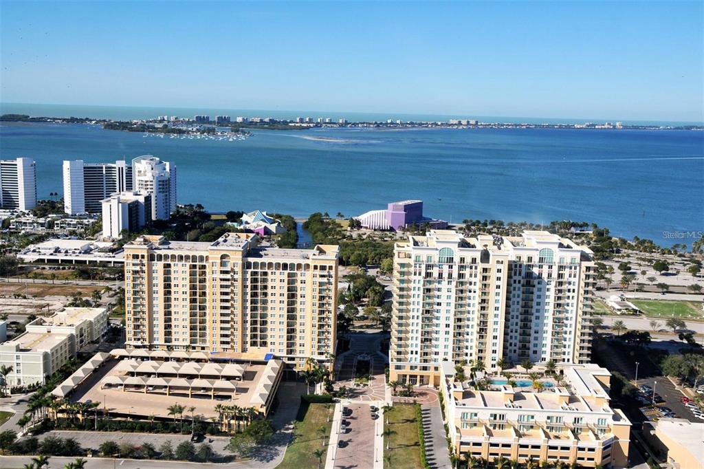 An aerial view shows two large residential buildings situated near a bay and beach — 750 N TAMIAMI TRAIL UNIT 916, SARASOTA, FL