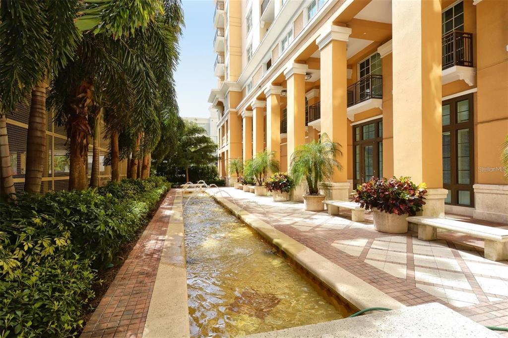 A long water feature runs alongside a paved walkway lined with columns and potted plants — 750 N TAMIAMI TRAIL UNIT 916, SARASOTA, FL