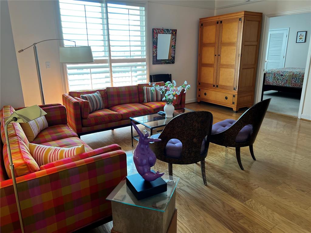 A living room features plaid sofas, two purple chairs, a glass coffee table, and wood flooring — 750 N TAMIAMI TRAIL UNIT 916, SARASOTA, FL