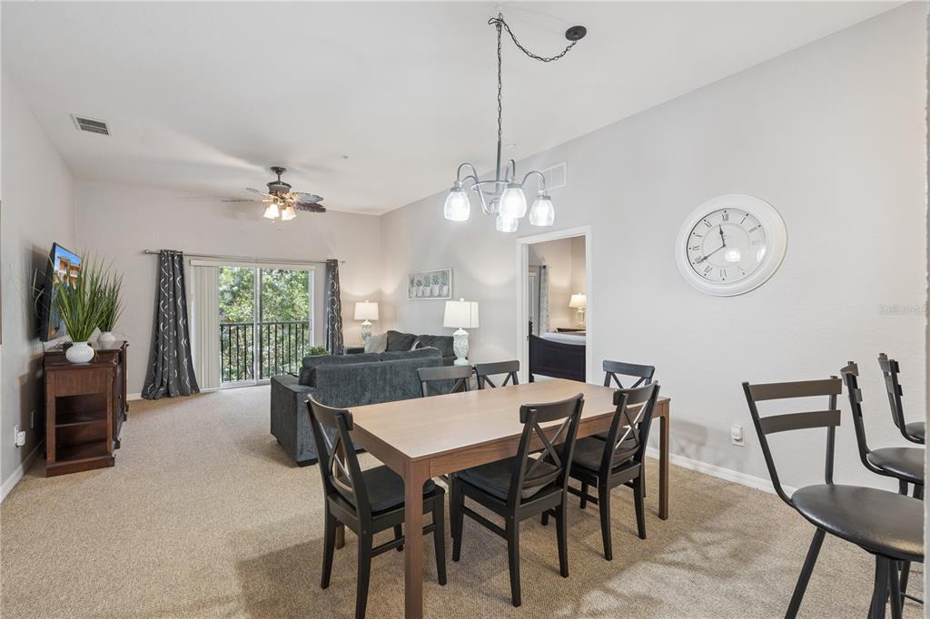 A dining area with a wooden table and chairs opens into a carpeted living room — 113 ANDROS AVENUE UNIT B16 U113, DAVENPORT, FL