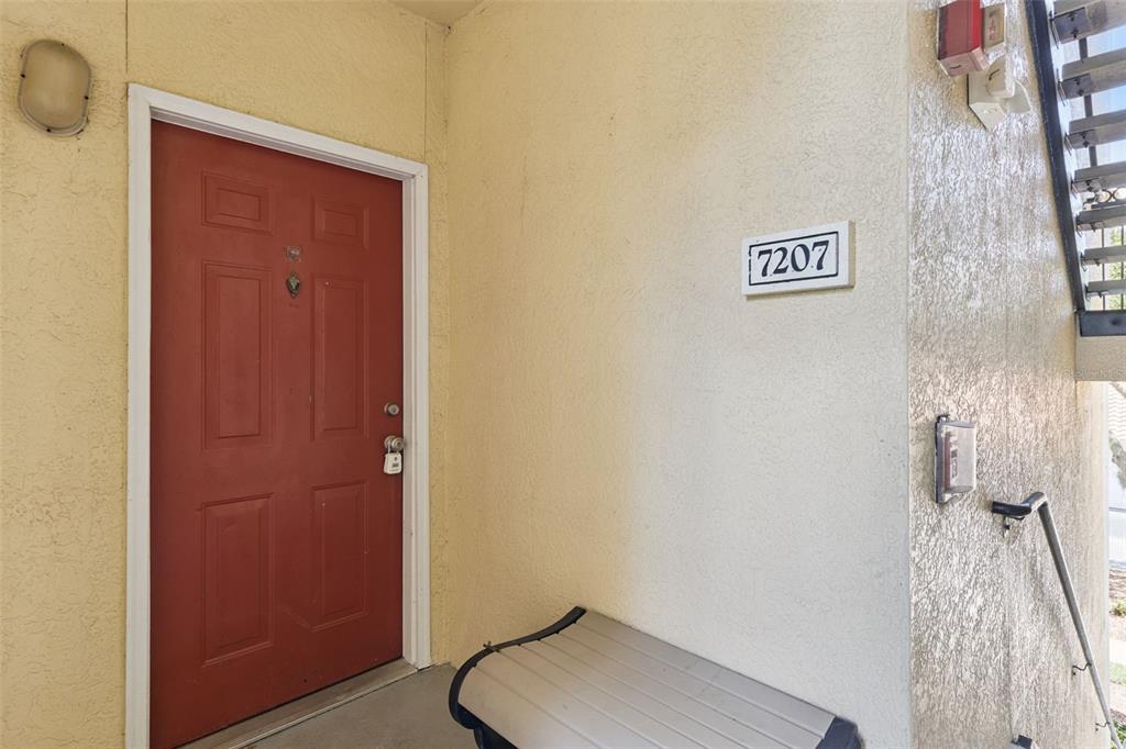 A red front door is adjacent to a wall with a 7207 unit number sign — 1460 LAKE SHADOW CIRCLE UNIT 7207, MAITLAND, FL