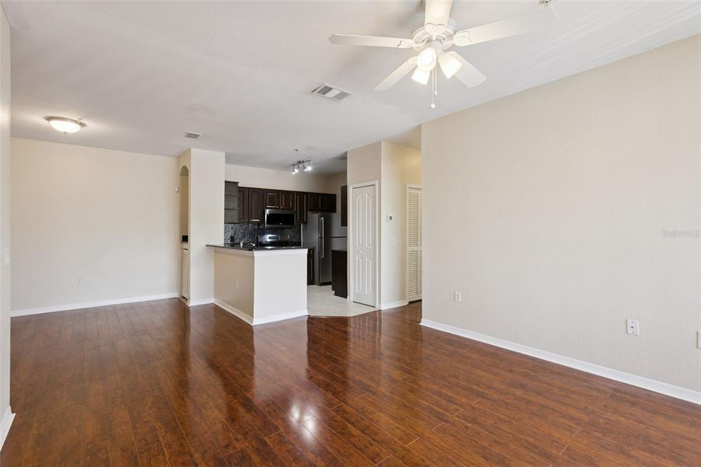 An open-concept living area features dark wood flooring, a ceiling fan, and an adjacent kitchen — 1460 LAKE SHADOW CIRCLE UNIT 7207, MAITLAND, FL