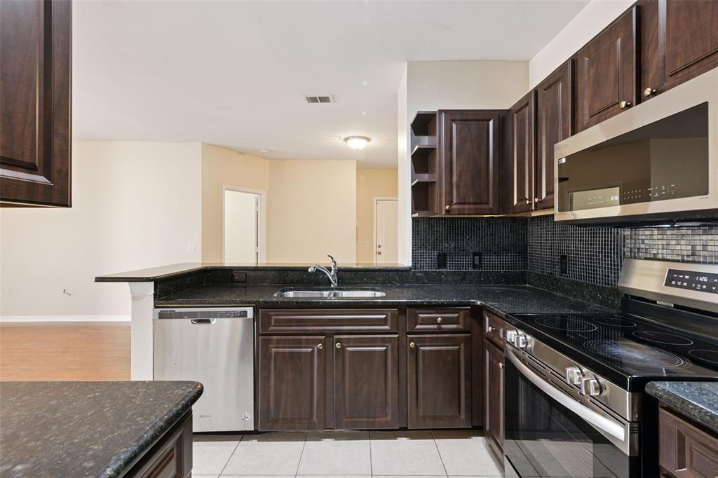 A kitchen features dark wood cabinets, black granite countertops, stainless steel appliances, and tile flooring — 1460 LAKE SHADOW CIRCLE UNIT 7207, MAITLAND, FL