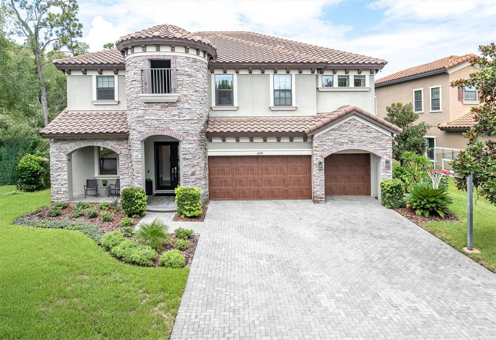 A two-story house with a stone-clad turret, tiled roof, and a paved driveway — 3099 BARBOUR TRAIL, ODESSA, FL