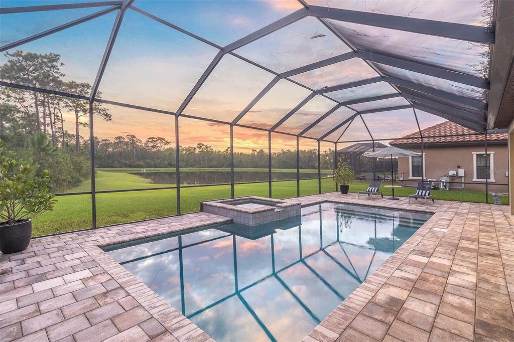 A screened-in pool and spa area with paver decking overlooking a pond at sunset — 3099 BARBOUR TRAIL, ODESSA, FL