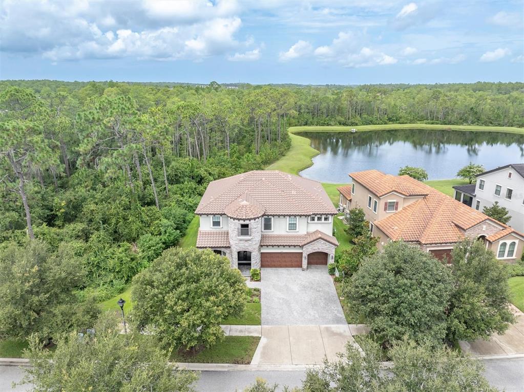 An aerial view shows a two-story house with a tile roof next to a lake — 3099 BARBOUR TRAIL, ODESSA, FL
