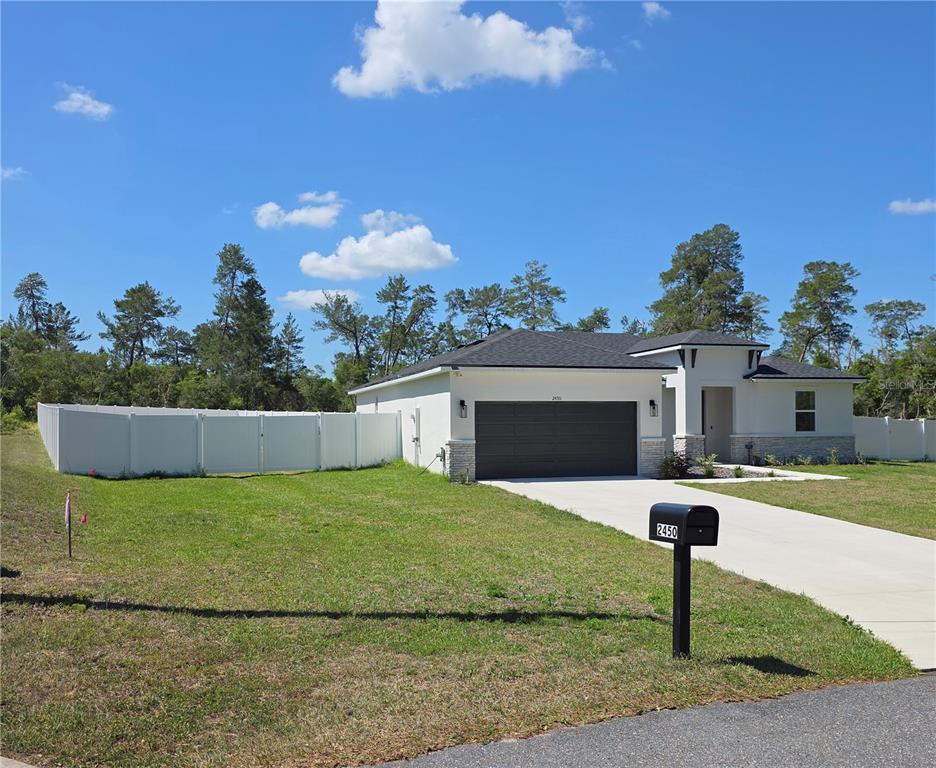 A single-story house with a dark garage door, stone accents, and a white vinyl fence — 2450 SW 170TH LOOP, OCALA, FL