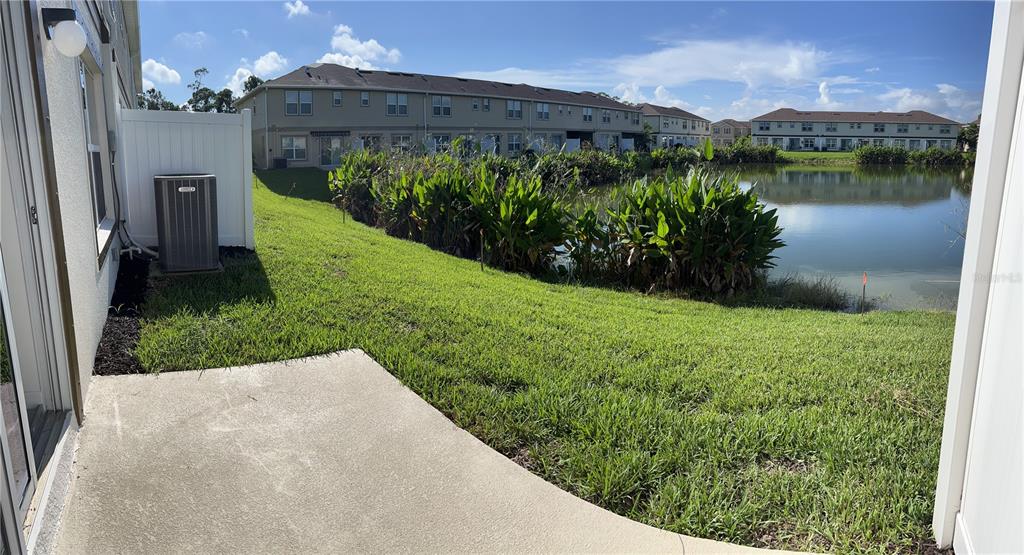A concrete patio overlooks a grassy lawn, a pond, and multi-story residential buildings — 15031 CASPIAN TERN COURT UNIT 105, NORTH FORT MYERS, FL