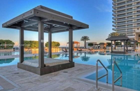 A poolside cabana with a cushioned daybed sits on a stone deck by a pool — 1830 S Ocean Dr # 1705, Hallandale Beach FL 33009, HALLANDALE BEACH, FL