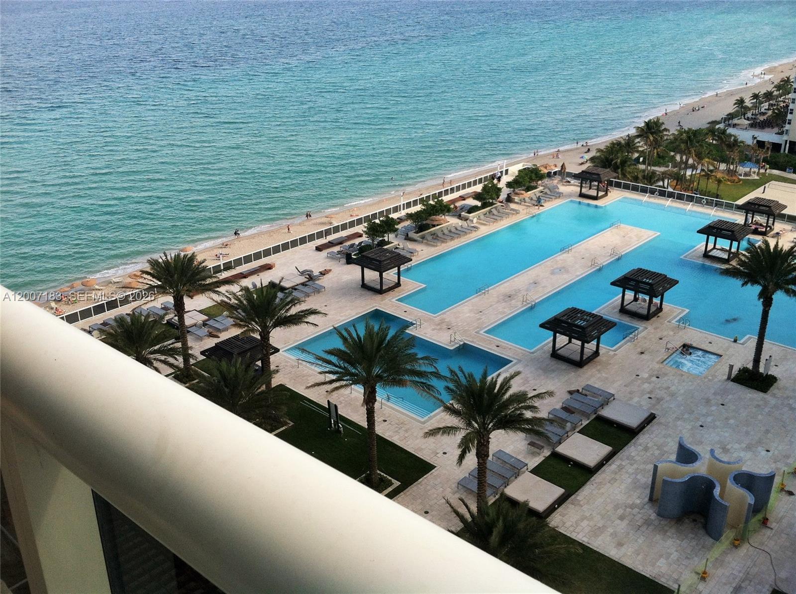 An elevated view of a resort-style swimming pool complex adjacent to a sandy beach — 1830 S Ocean Dr # 1705, Hallandale Beach FL 33009, HALLANDALE BEACH, FL