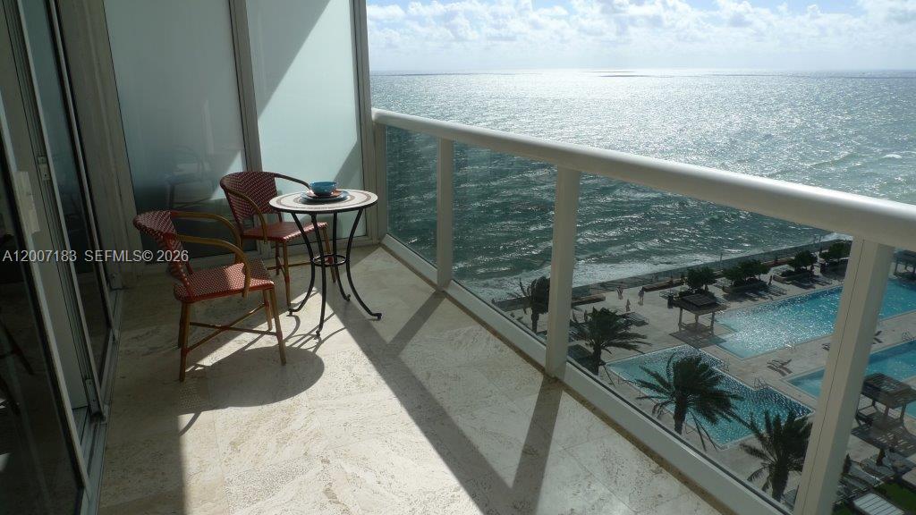A balcony with a small table and two chairs overlooks the ocean and a pool — 1830 S Ocean Dr # 1705, Hallandale Beach FL 33009, HALLANDALE BEACH, FL