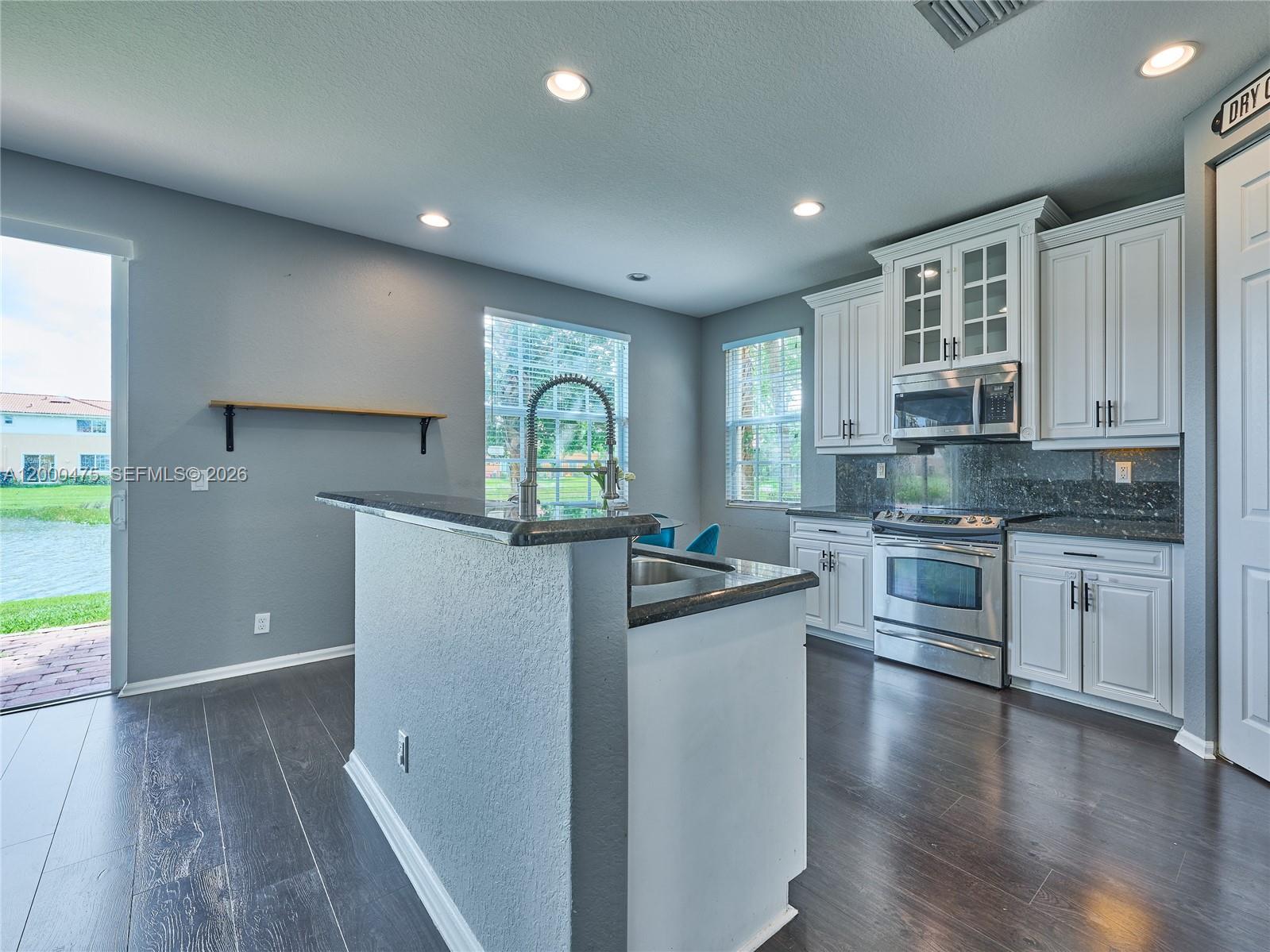 A kitchen features white cabinets, dark countertops, stainless steel appliances, and dark wood flooring — 7430 Briella Dr, Boynton Beach FL 33437, BOYNTON BEACH, FL