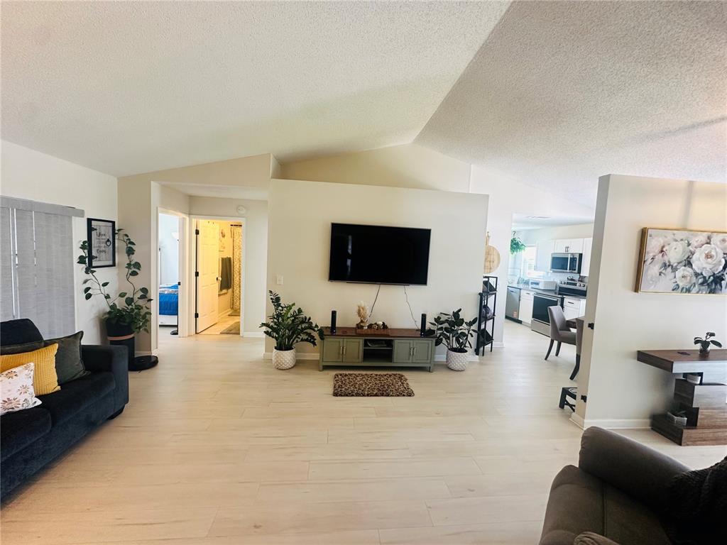 A living room with light wood-look tile floors, a wall-mounted television, and an open kitchen — 340 EDGEWOOD COURT, KISSIMMEE, FL