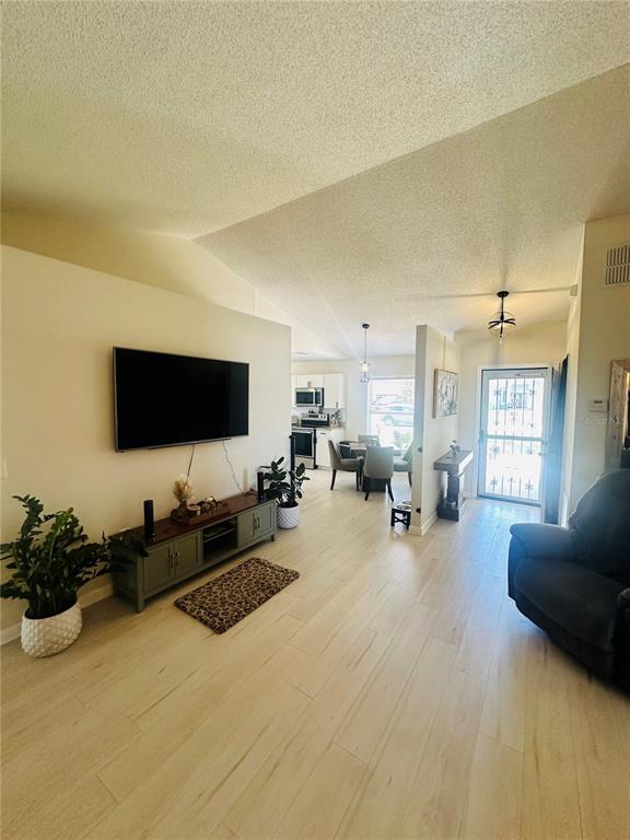 A living room with light wood floors, a wall-mounted television, and an open kitchen view — 340 EDGEWOOD COURT, KISSIMMEE, FL