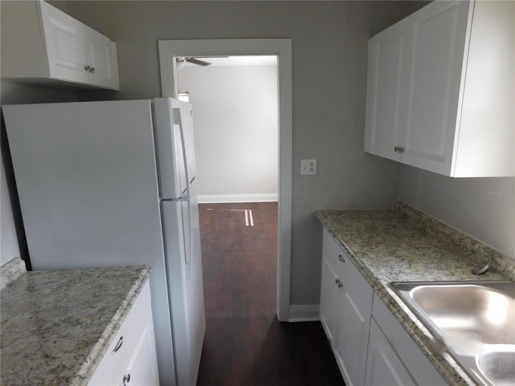 A kitchen with white cabinets, granite countertops, and a white refrigerator leads to another room — 7383 WAVERLY ROAD UNIT #1, LAKE WALES, FL