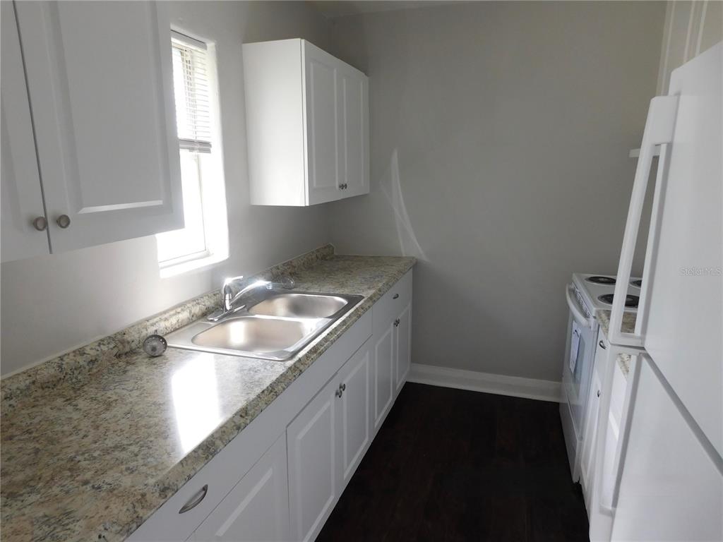 A galley kitchen features white cabinets, granite-look countertops, a double sink, and white appliances — 7383 WAVERLY ROAD UNIT #1, LAKE WALES, FL