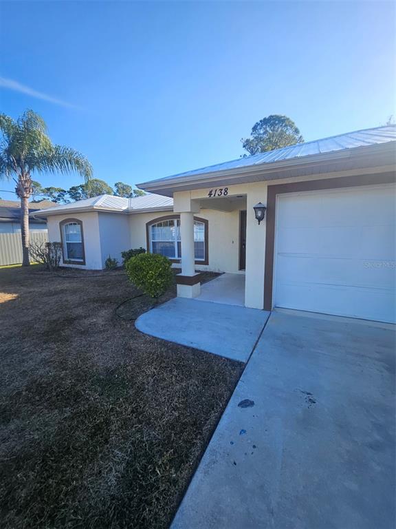 A single-story house with a white garage door, tan stucco walls, and a metal roof — 4138 AZORA STREET, NORTH PORT, FL