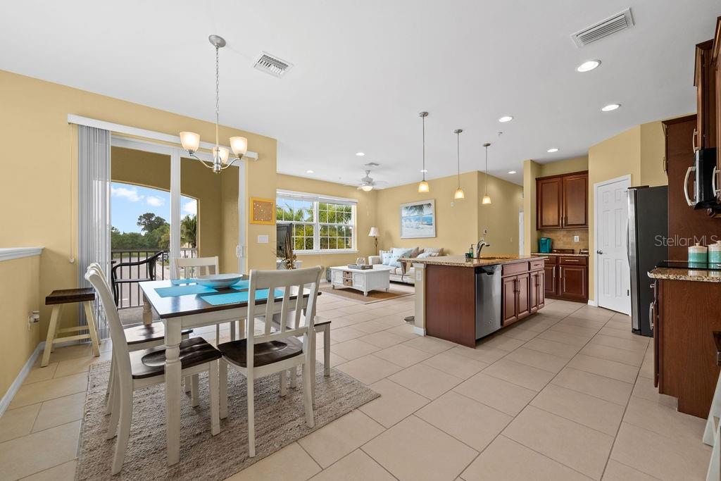 An open-concept kitchen and dining area with tile flooring, dark wood cabinets, and pendant lighting — 184 EXPLORER DRIVE, OSPREY, FL