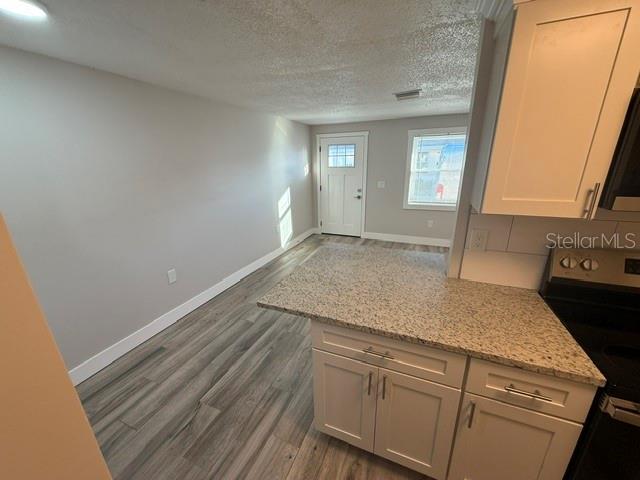 A kitchen with granite countertops and white cabinets overlooks a room with light-colored flooring — 4933 ELKNER STREET, NEW PORT RICHEY, FL