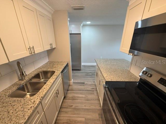 A kitchen features white cabinets, granite countertops, stainless steel appliances, and wood-look flooring — 4933 ELKNER STREET, NEW PORT RICHEY, FL