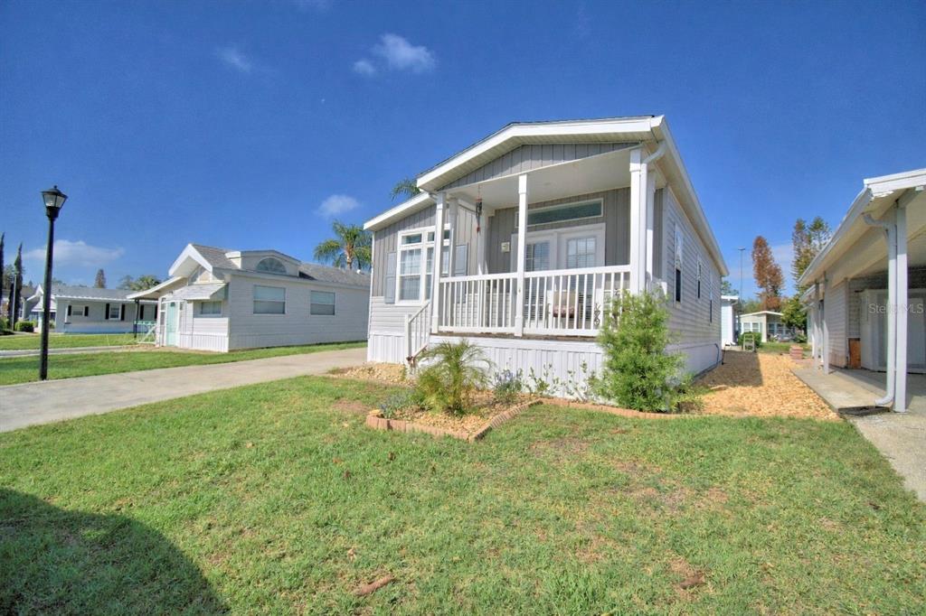 A light gray manufactured home features a front porch and a small landscaped garden bed — 4925 CYPRESS GARDENS ROAD UNIT 100, WINTER HAVEN, FL