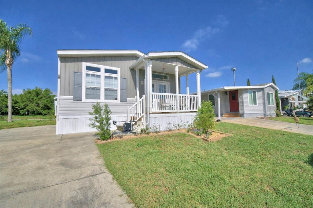 A light gray manufactured home features a front porch, white railings, and a concrete driveway — 4925 CYPRESS GARDENS ROAD UNIT 100, WINTER HAVEN, FL