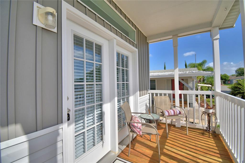A covered wooden porch features two chairs, a small table, and white French doors — 4925 CYPRESS GARDENS ROAD UNIT 100, WINTER HAVEN, FL