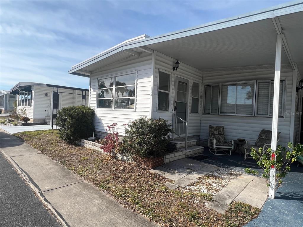 A white mobile home with a covered porch and a paved walkway sits on a lot — 354 KING PALM STREET, LARGO, FL