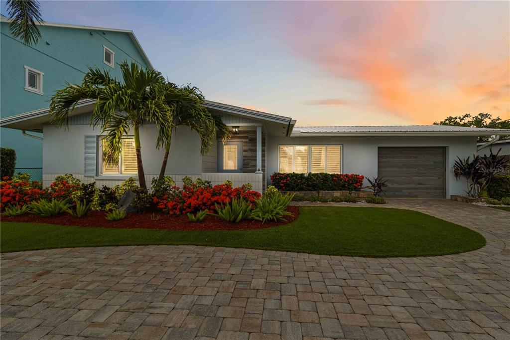 A single-story house with a paved driveway, palm tree, and vibrant landscaping at sunset — 720 IXORA AVENUE, ELLENTON, FL