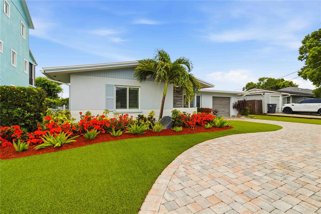 A light blue house with a paver driveway, artificial turf, and vibrant red landscaping — 720 IXORA AVENUE, ELLENTON, FL