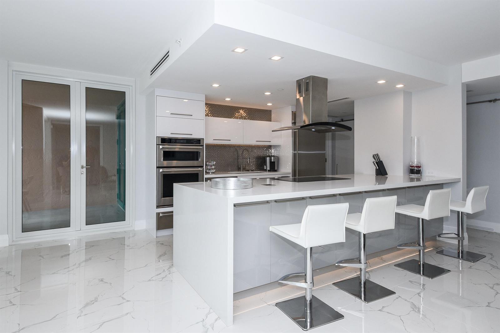 A modern kitchen features a white waterfall island, stainless steel appliances, and marble-patterned tile flooring — 120 SE 5th Avenue, Boca Raton FL 33432, BOCA RATON, FL