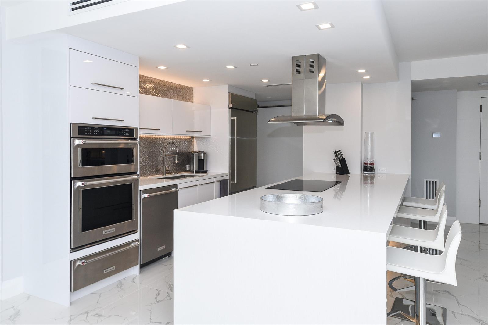 A modern white kitchen features a large island, stainless steel appliances, and marble-patterned tile flooring — 120 SE 5th Avenue, Boca Raton FL 33432, BOCA RATON, FL